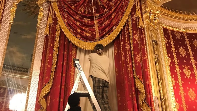 Lucie stood on a ladder, cleaning the silk curtains in the Saloon 