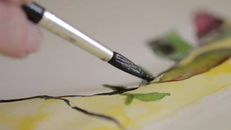 A close-up of a paint brush moving across a watercolour painting