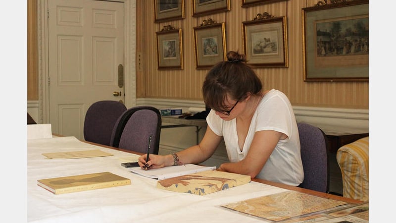 Student leaning over books and archive material and using it to draw designs