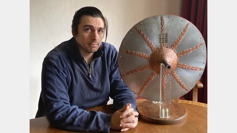 Andrew Braund sat at a table. Next to him is the gun shield replica.